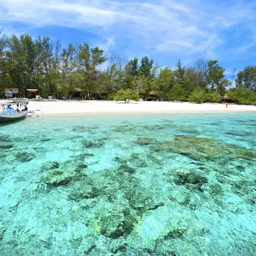 A boat docks in clear water at a beach in Indonesia.