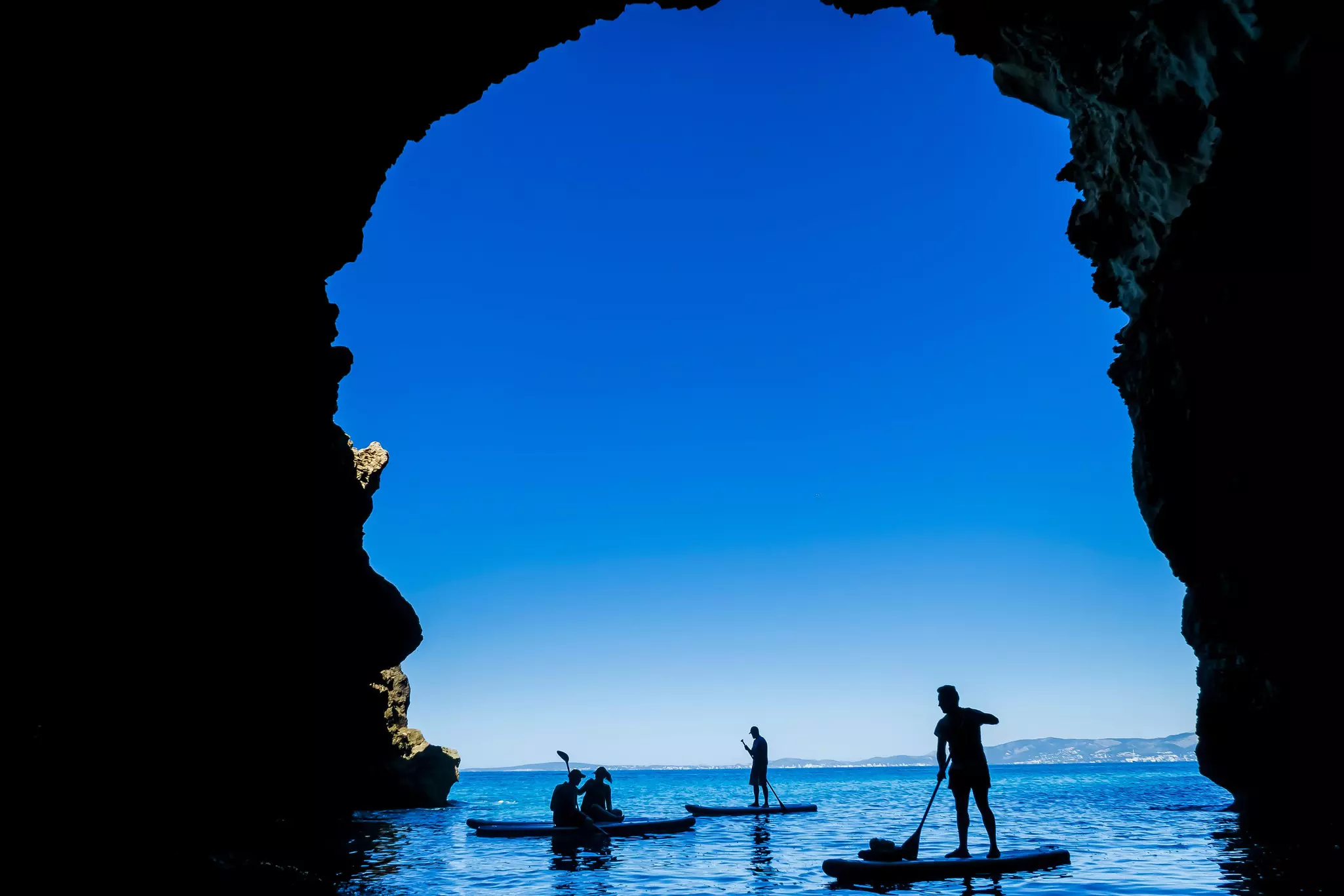 People on paddleboards in silhouette in a sea cave in Mallorca, Spain