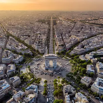An aerial view of the Arc de Triomphe in the evening sunset with many cars on the roads that fan out from this massive landmark