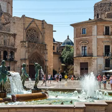 Water jets of the Fountain of the Turia play before the Gothic portal of Valencia Cathedral and the blue-tiled dome of the basilica.