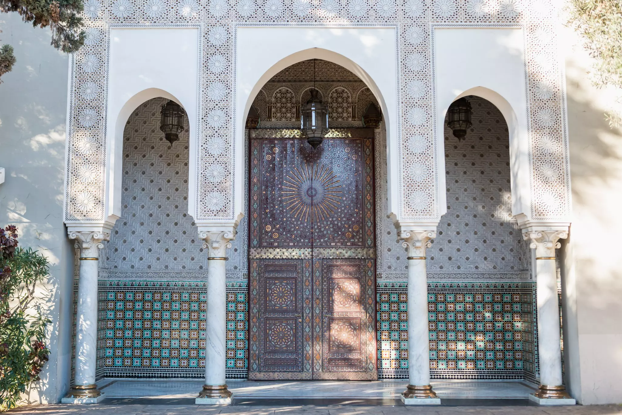An elaborately decorated wood door set back in an alcove covered in patterned tiles is reached through an archway with four carved columns.