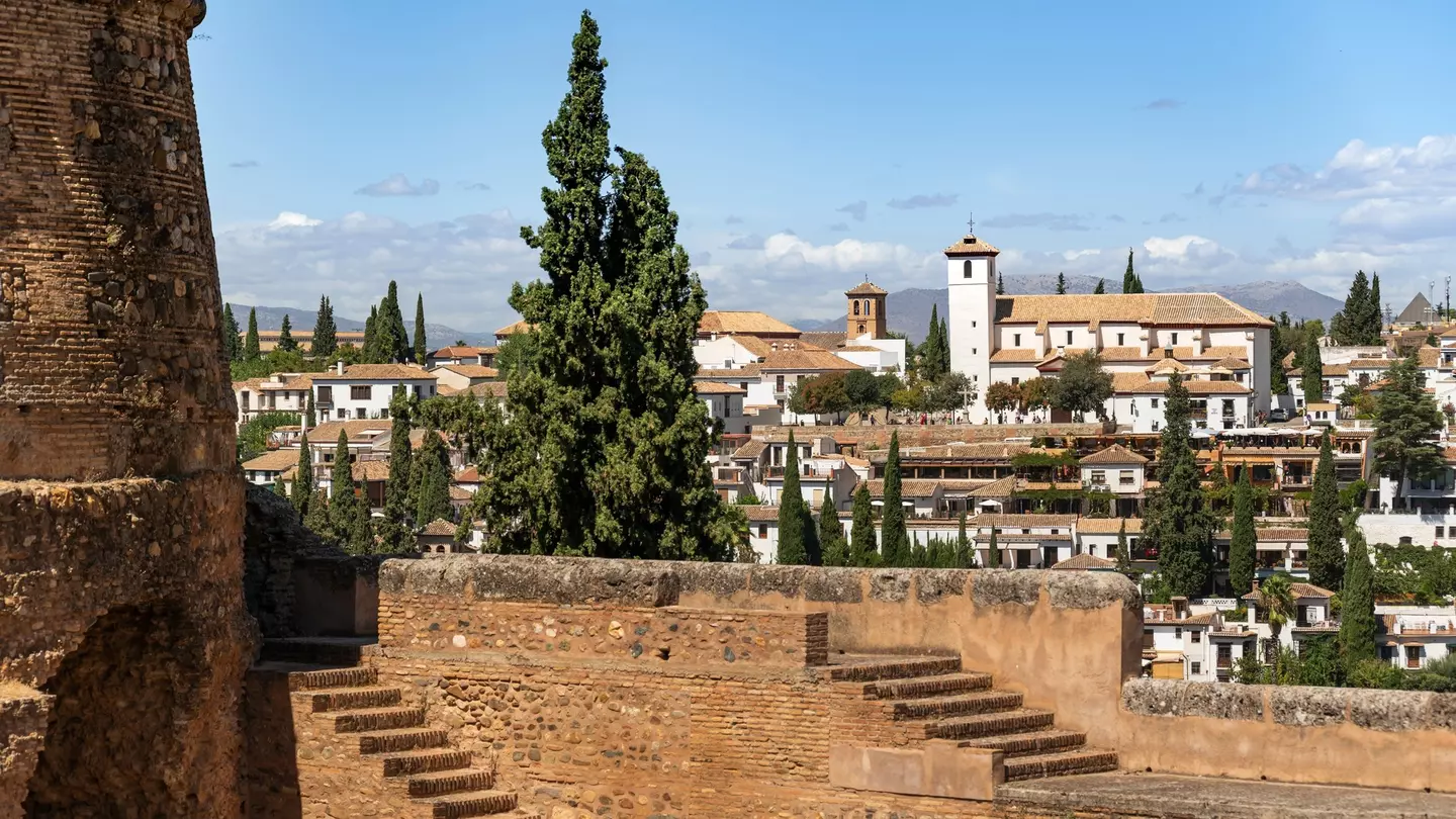 White buildings on a hillside are seen from the ramparts of a stone fortress.