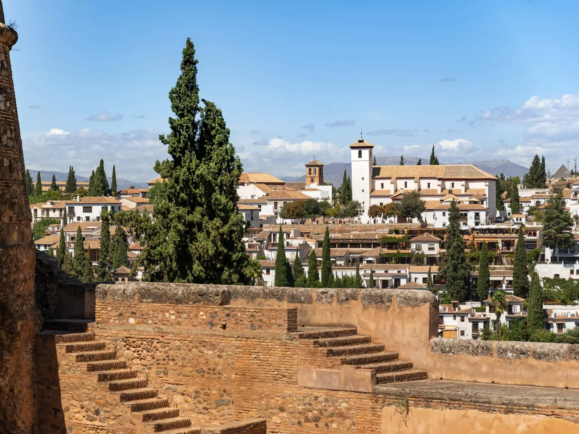 White buildings on a hillside are seen from the ramparts of a stone fortress.