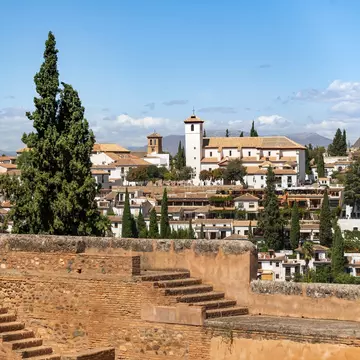 White buildings on a hillside are seen from the ramparts of a stone fortress.