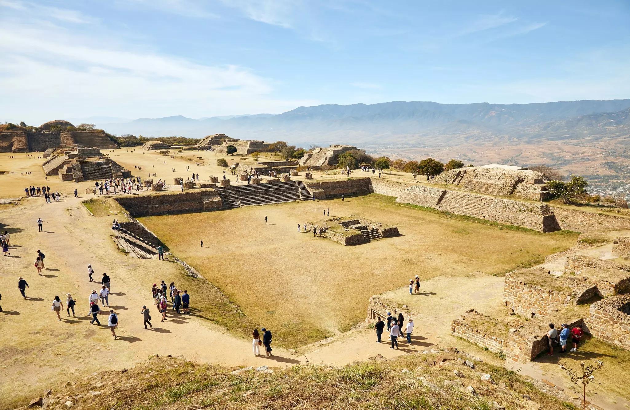 Aerial view of people walking around a large archaelogical site with stone ruins on a sunny day.