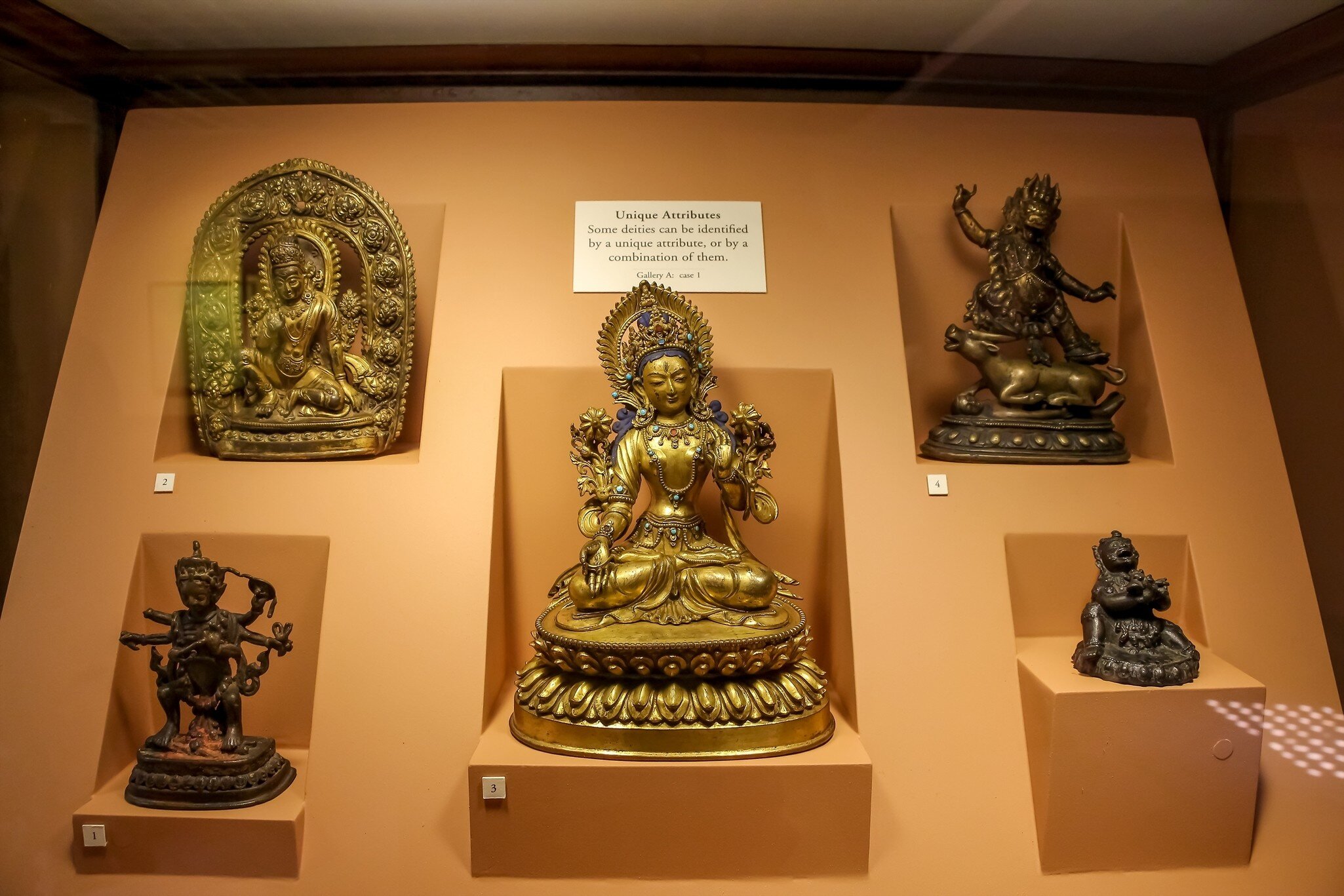 Nepal, Lalitpur - May 10, 2019: Group of bronze Buddha and Hindu Gods figurines on orange background in showcase of Patan Museum on Patan Durbar Square. Soft focus. Religious heritage theme.; Shutterstock ID 2273076965;