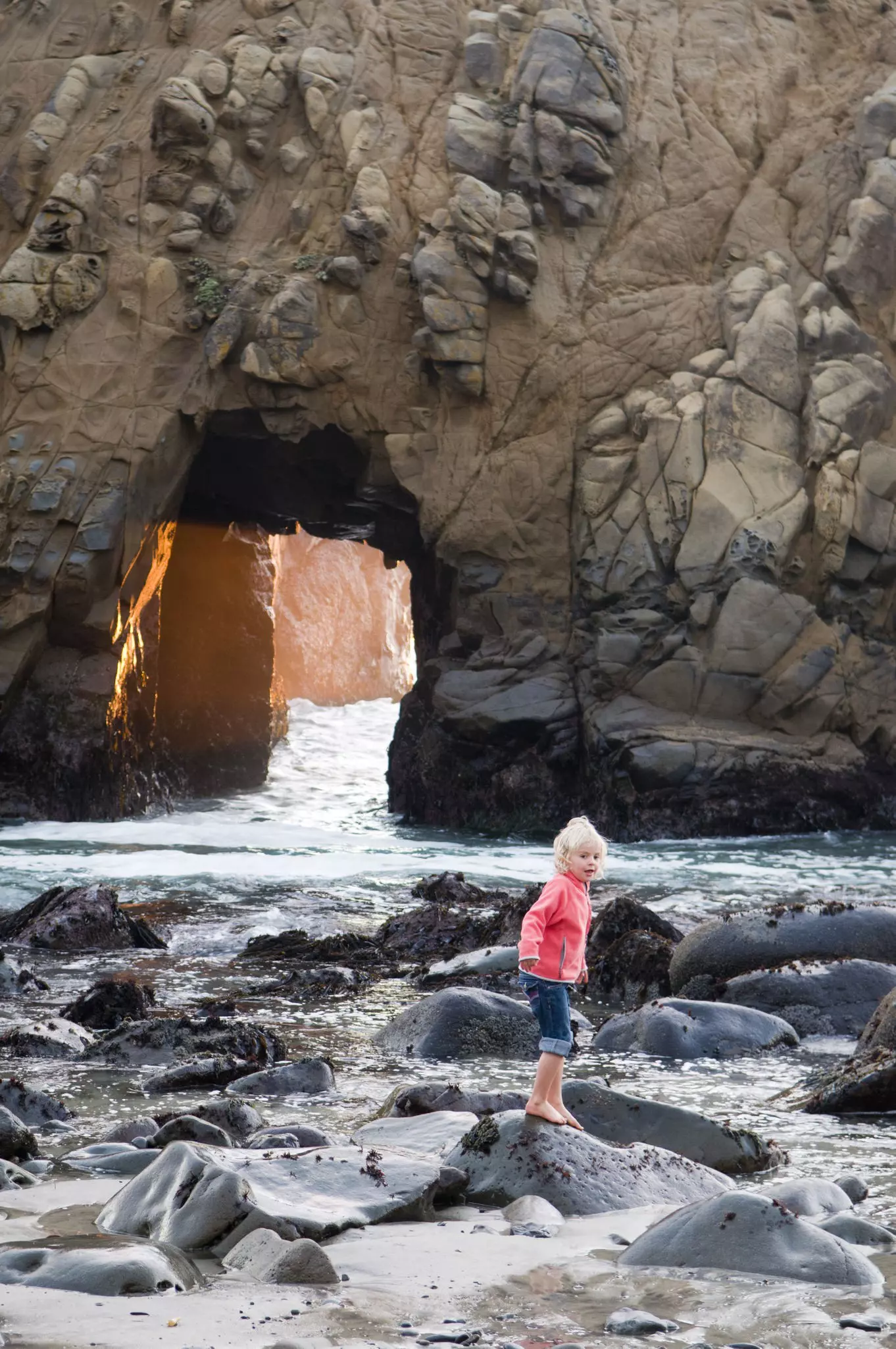 A young girl playing on coastal rocks near a blow hole in Big Sur.