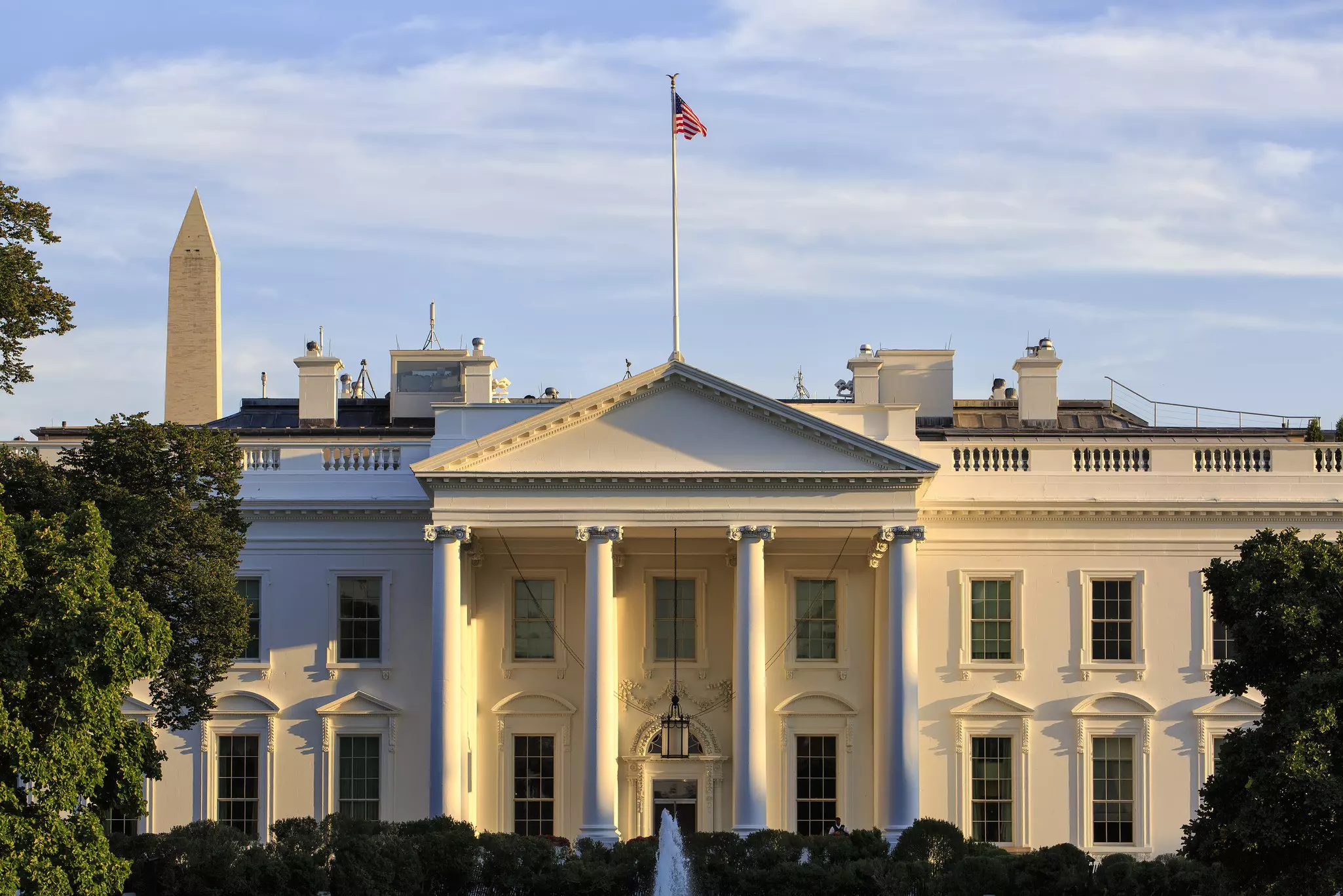 Exterior of the White House -- a large symmetrical colonnaded property with an American flag flying above it