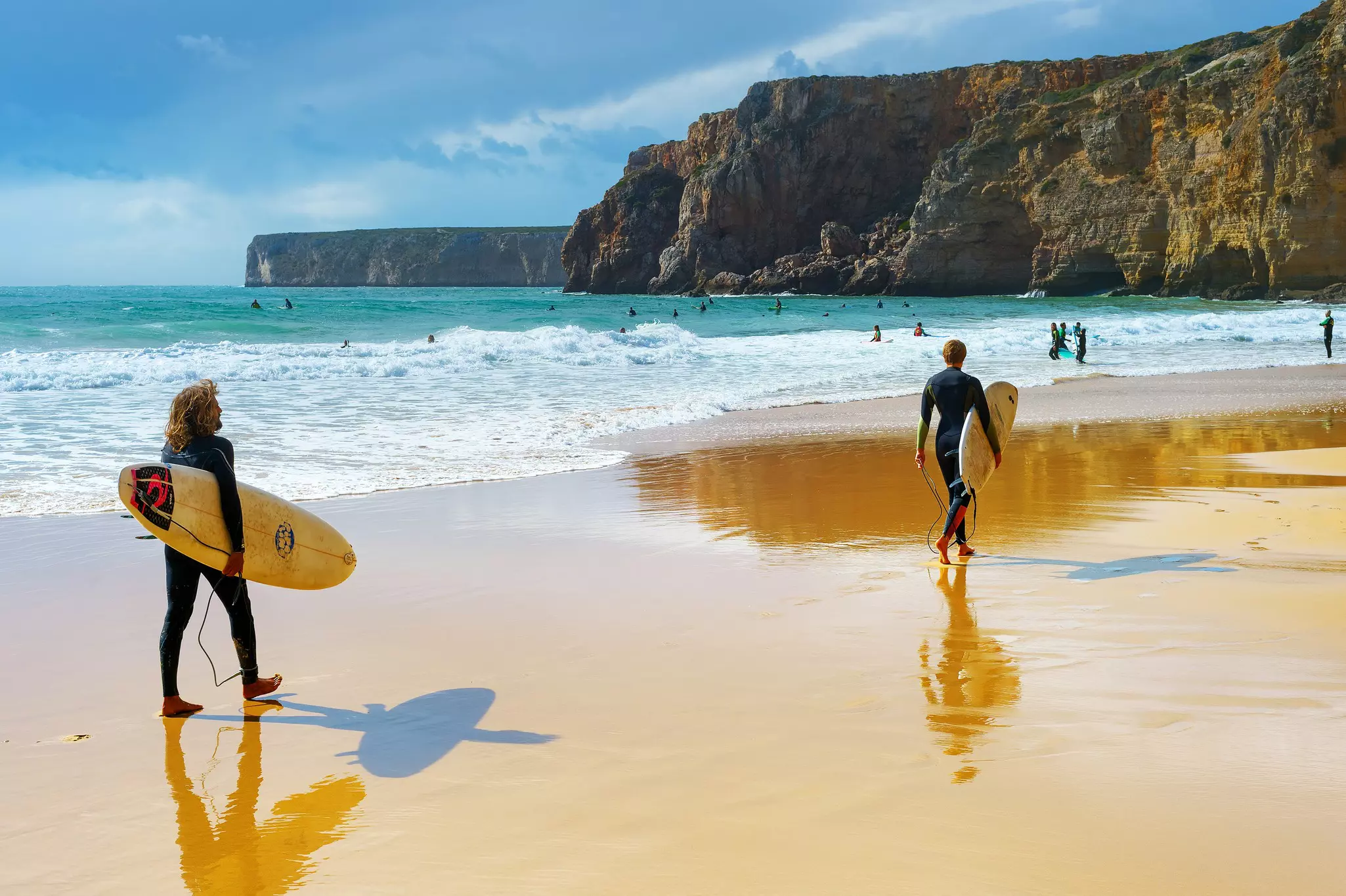 Young men walking by sandy beach with surfboard. Algarve is a famous surfing destination in Portugal.