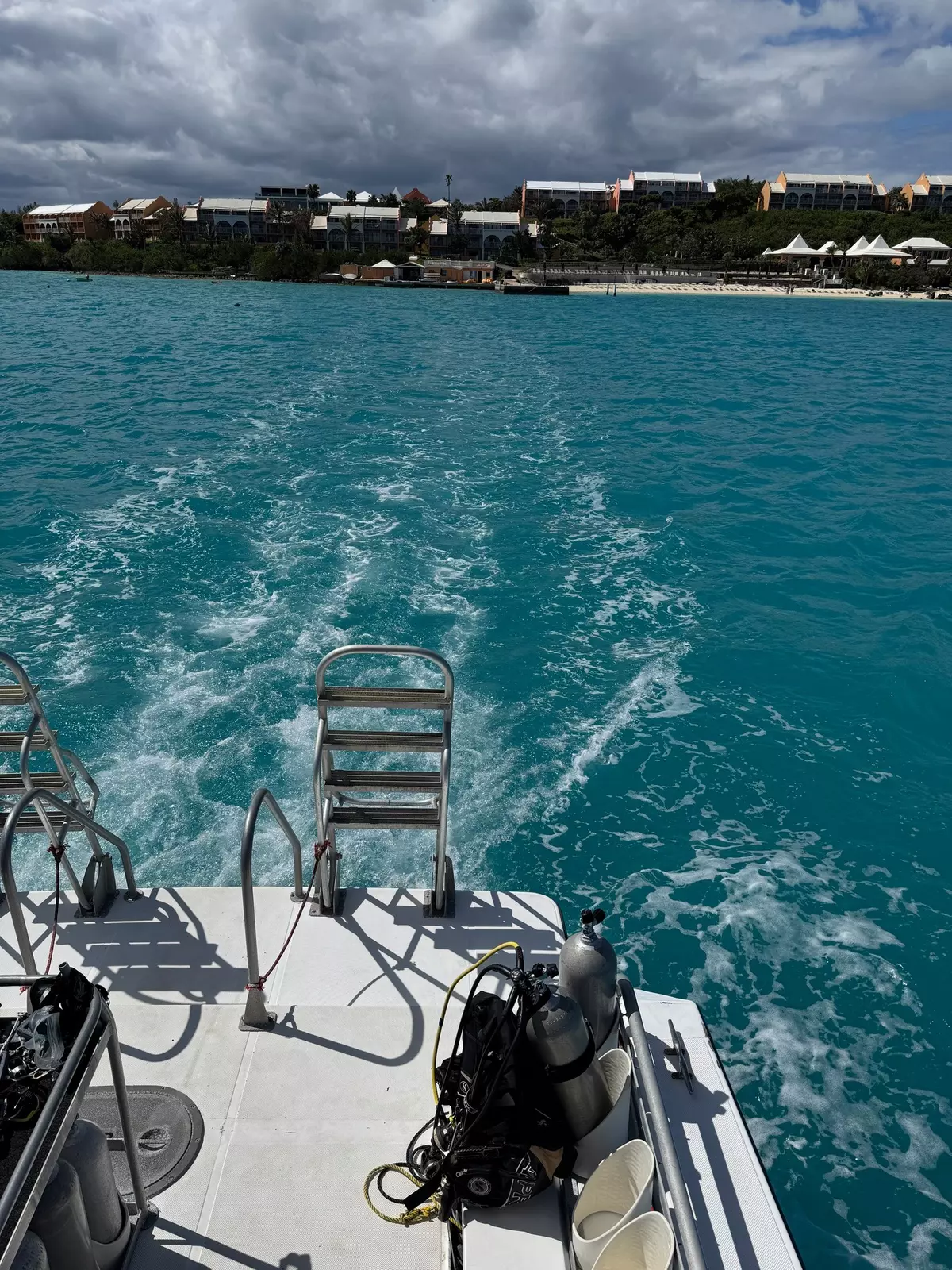 The wake of a boat in blue water as it pulls away from the far shore.