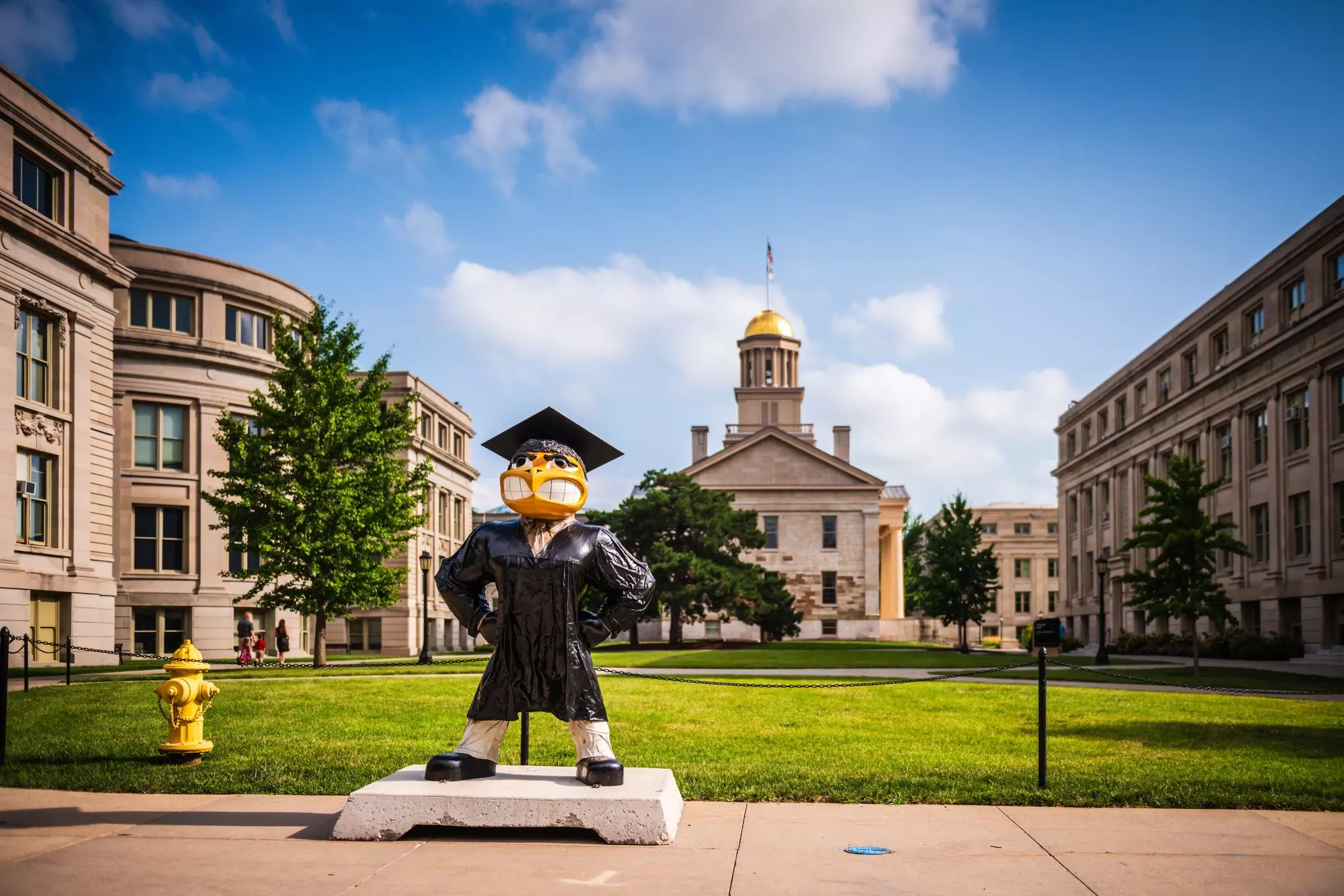 A statue of an eagle mascot is on the sidewalk in front of grand buildings in a town.