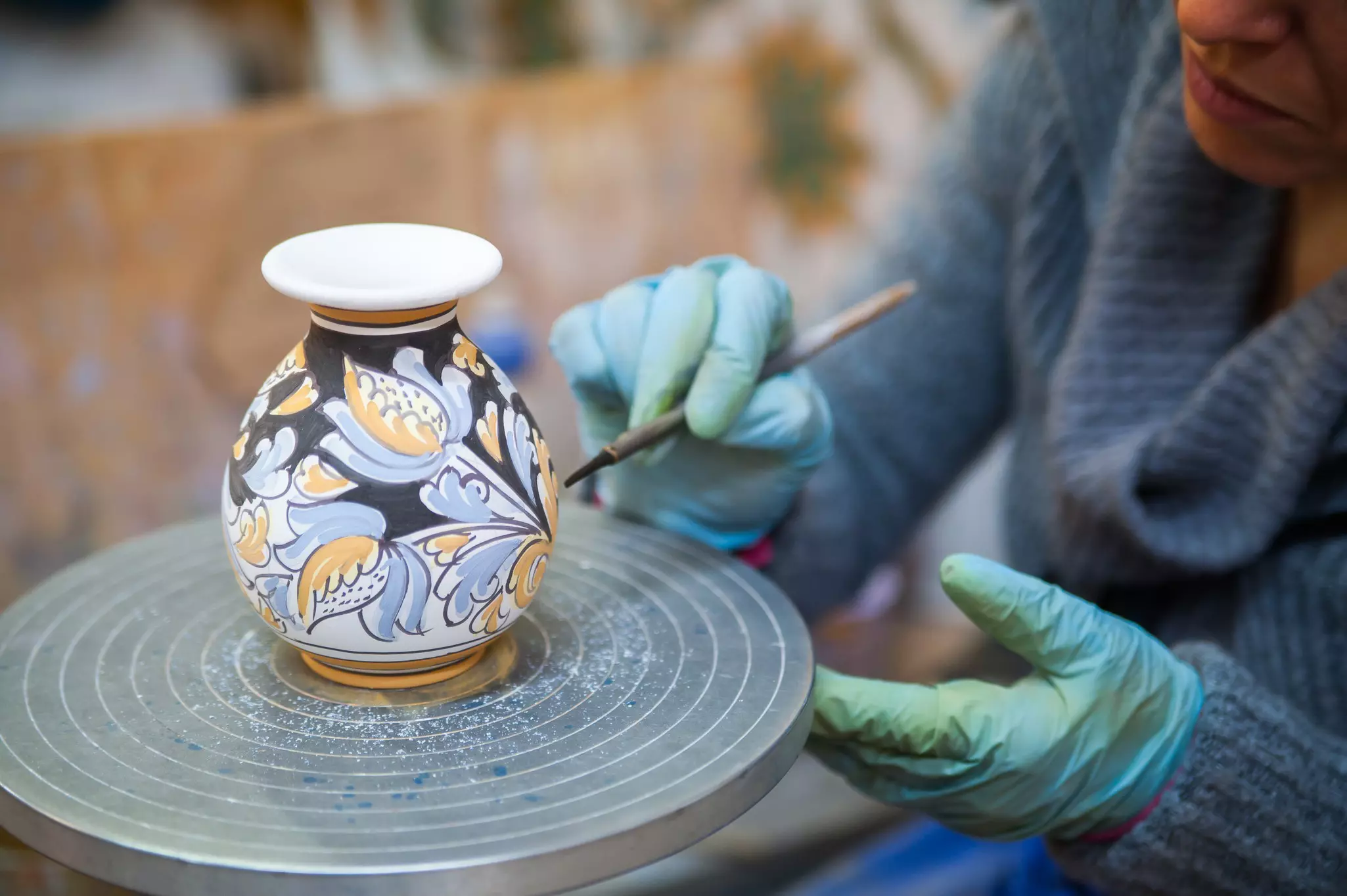 View of a ceramic vase on a potter's wheel being decorated by a local artisan with a paintbrush.
