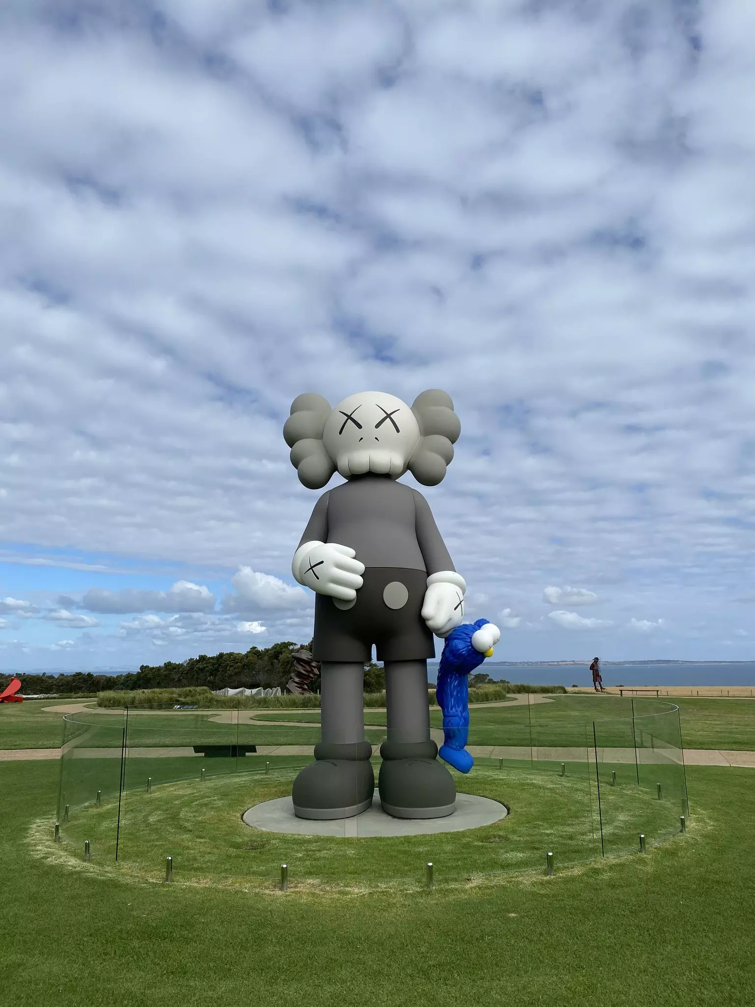 Shelves of books and a make-shift scare-crow wearing a skippers hat and white shirt covered in decorative pins stand in front of a car at the market; Table Mountain is the background.