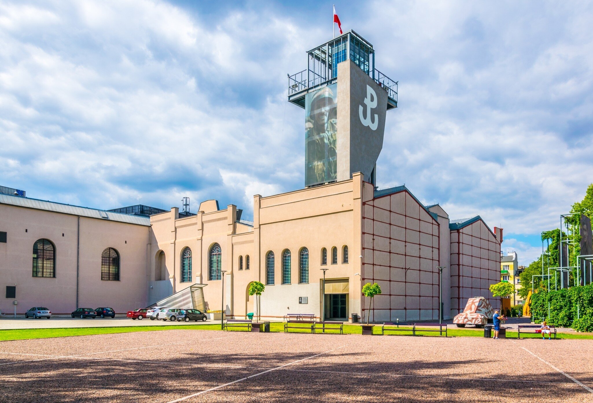 A brick museum building with a tall concrete tower carrying a white anchor emblem and a Polish flag.
