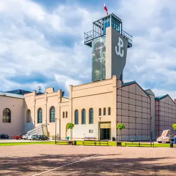 A brick museum building with a tall concrete tower carrying a white anchor emblem and a Polish flag.
