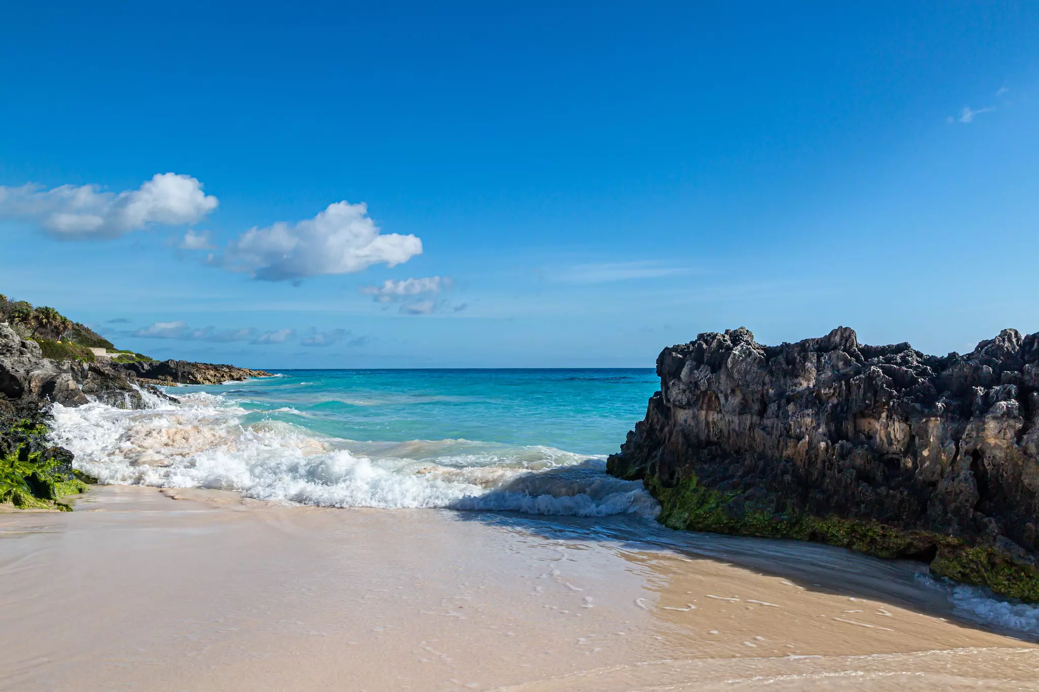 A rock-framed inlet lapped with waves approaching a golden-sand beach.