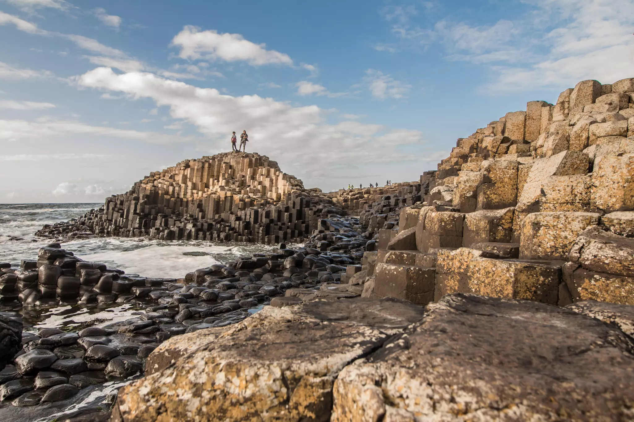 People standing and walking on huge columns and blocks of basalt rock on the coast