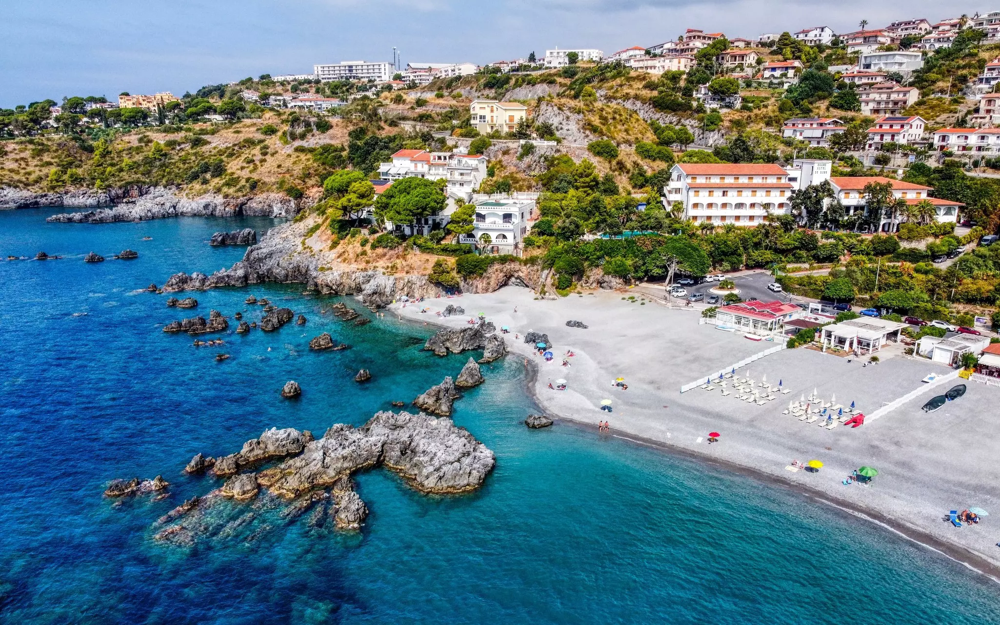 A hillside town with a wide sandy beach and several beachside restaurants.