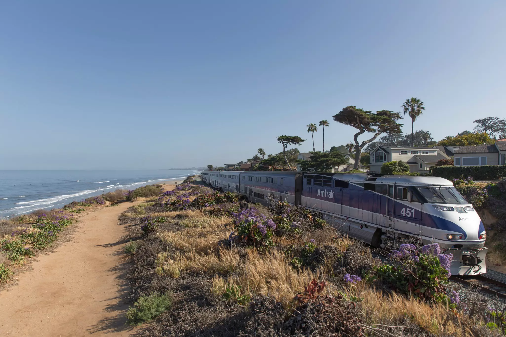 A train travels down a coastal track next to a beach.