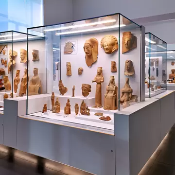 Glass cases of ancient terracotta heads, masks and figurines in a bright gallery of the museum in Reggio Calabria
