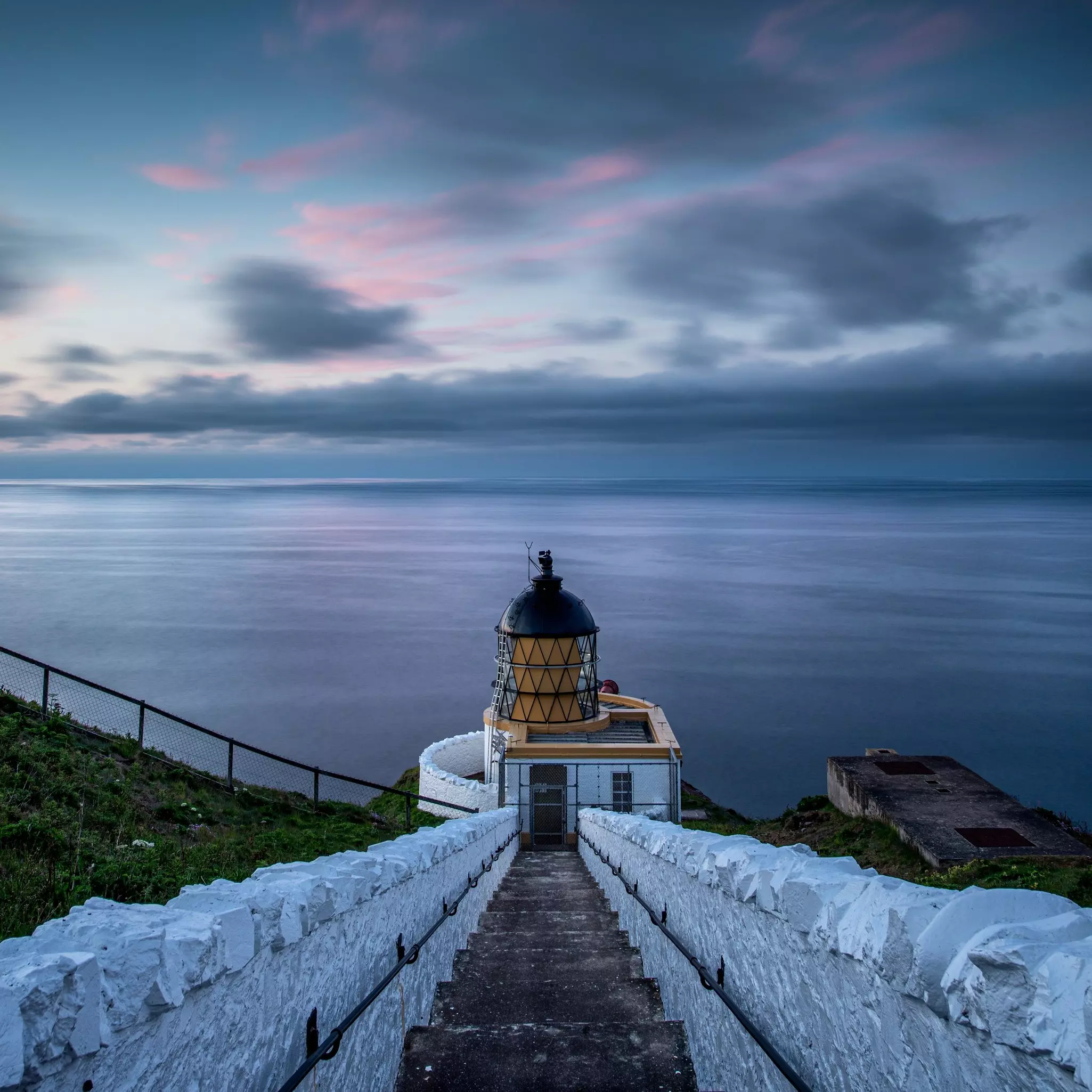 View of the stairs that descend to a lighthouse overlooking waters under a darkening sky