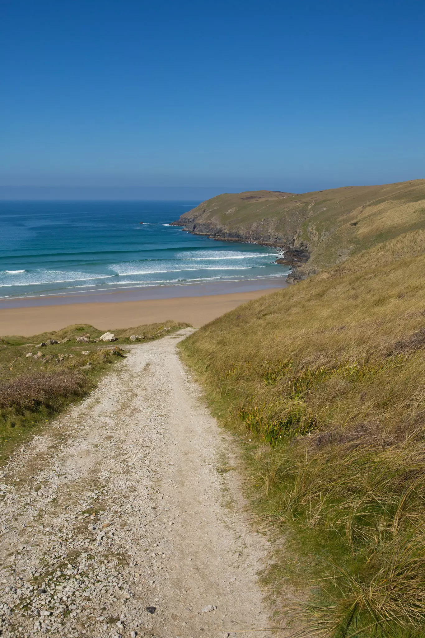A sandy path leading down form a cliff to a golden arc of sand.