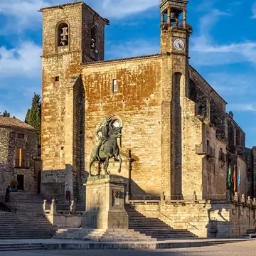 View of a statue and stone church on Plaza Mayor, the main square of Trujillo, Spain.
