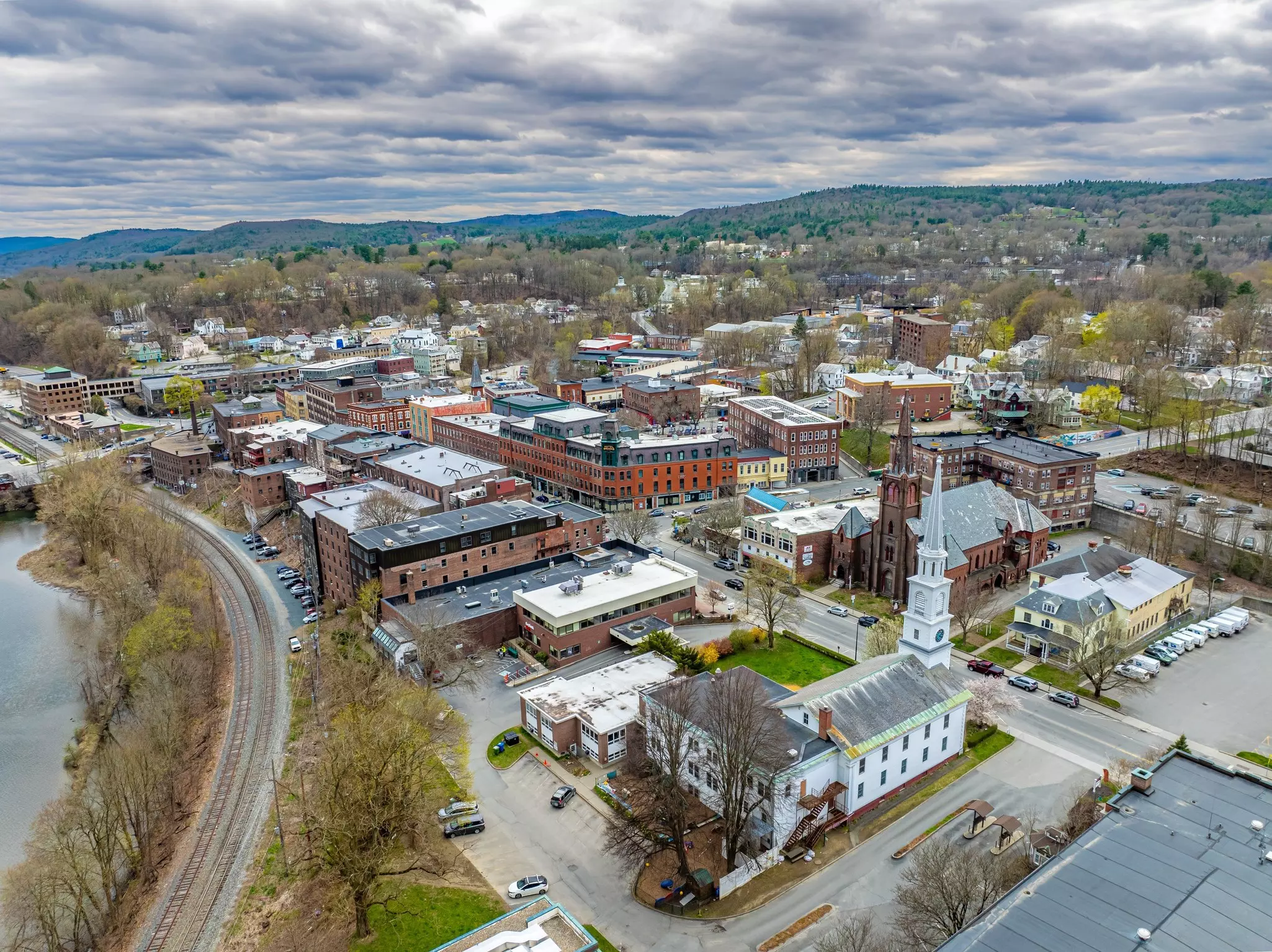 An aerial view of a town in Vermont; there is a white church with a tall steeple in the foreground and mountains on the horizon in the background.