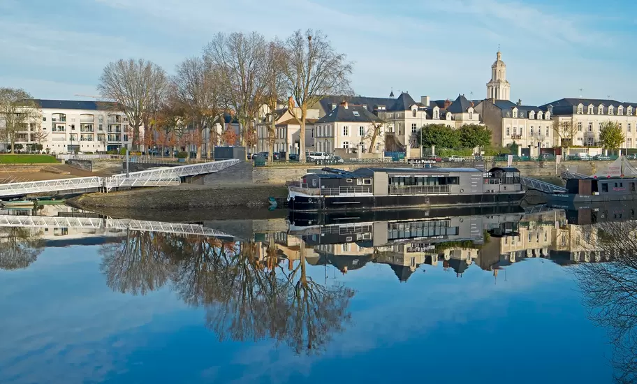 Barge restaurant La Péniche moored on the River Maine in Angers, townhouses and a bell tower reflected in still water