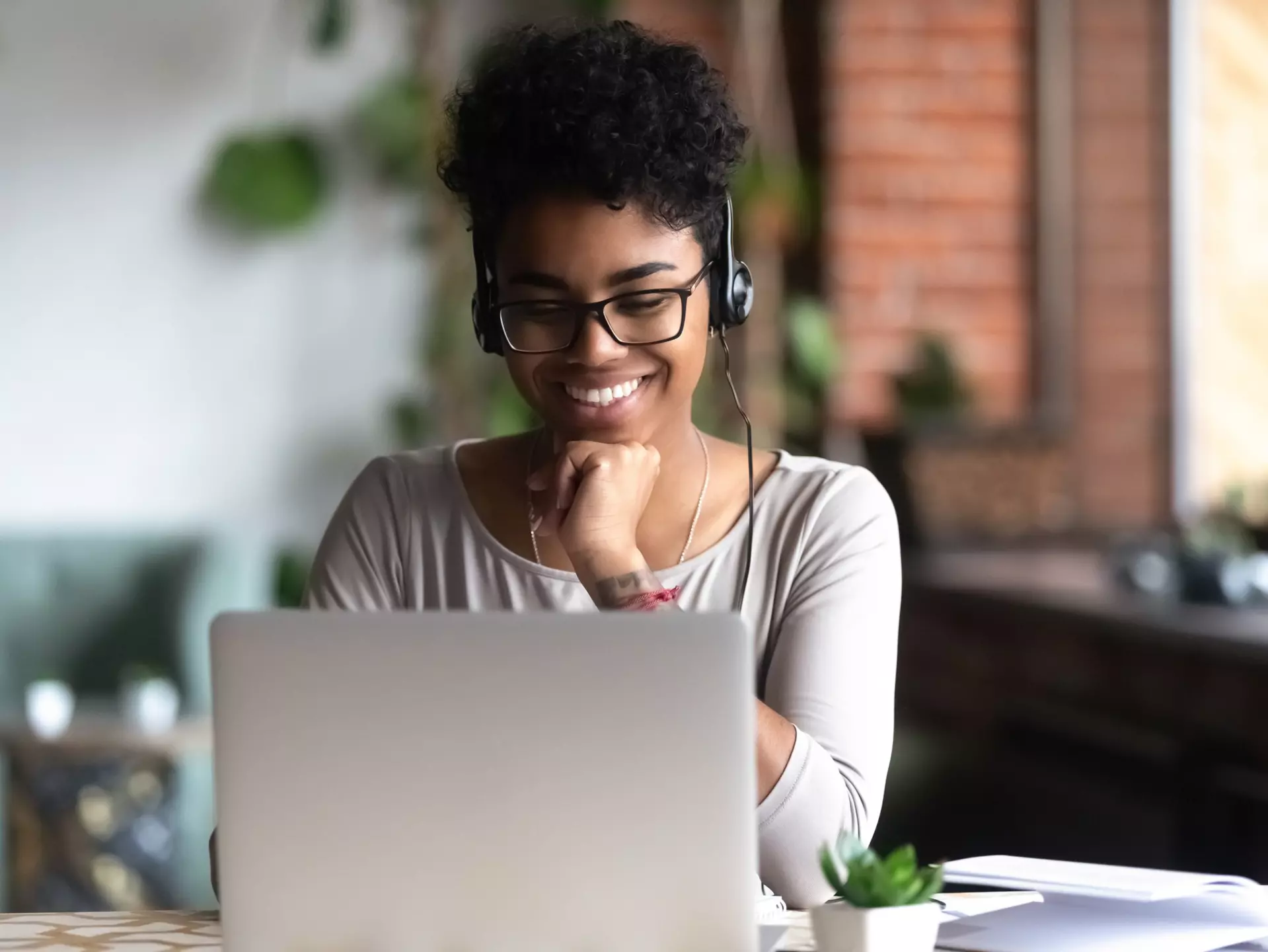 Black woman wearing headphones and smiling at her laptop