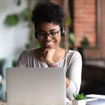 Black woman wearing headphones and smiling at her laptop
