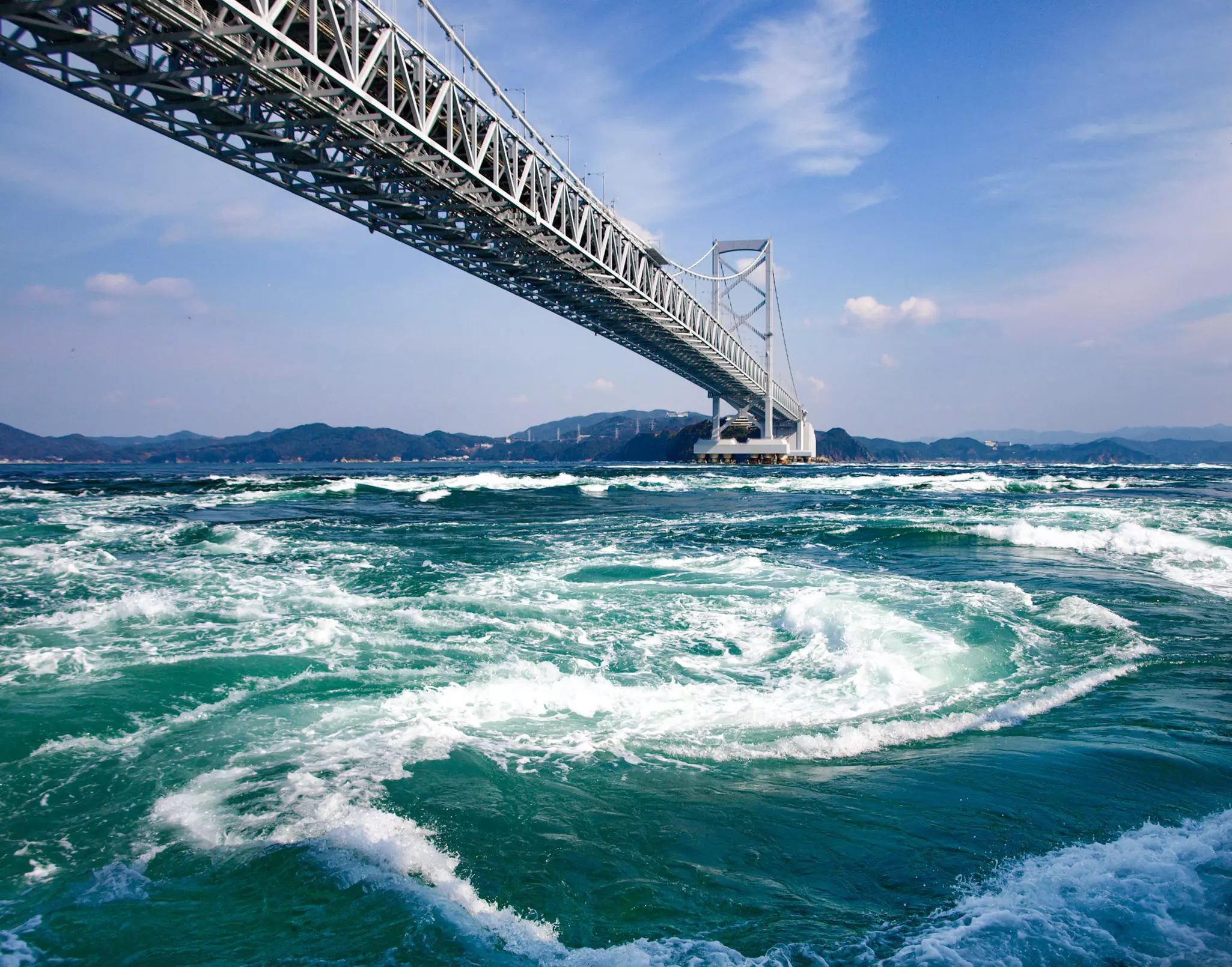 A massive churn of water in the ocean below a suspension bridge.
