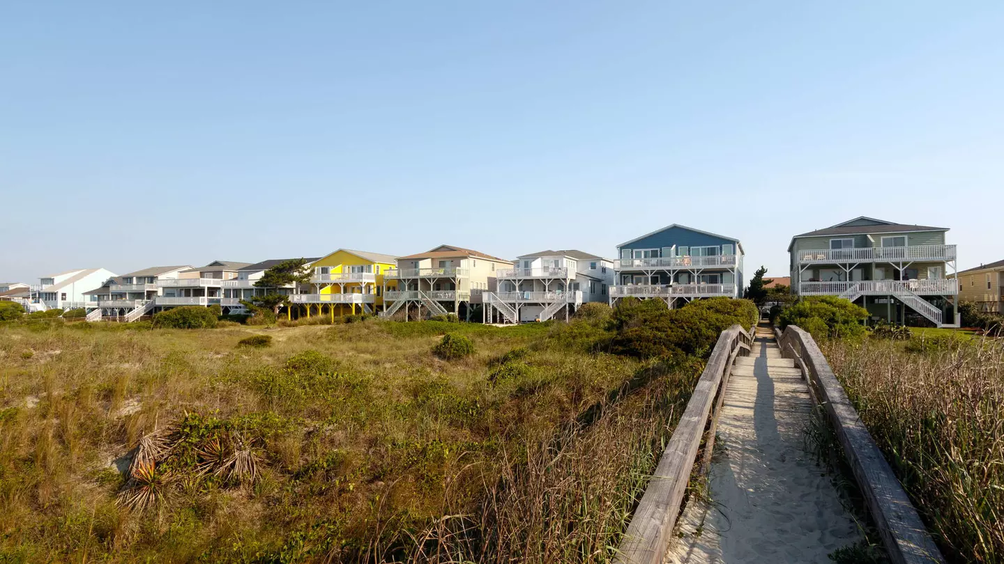 Beach houses across the green sand dunes with a long wooden walkway, Sunset Beach, North Carolina