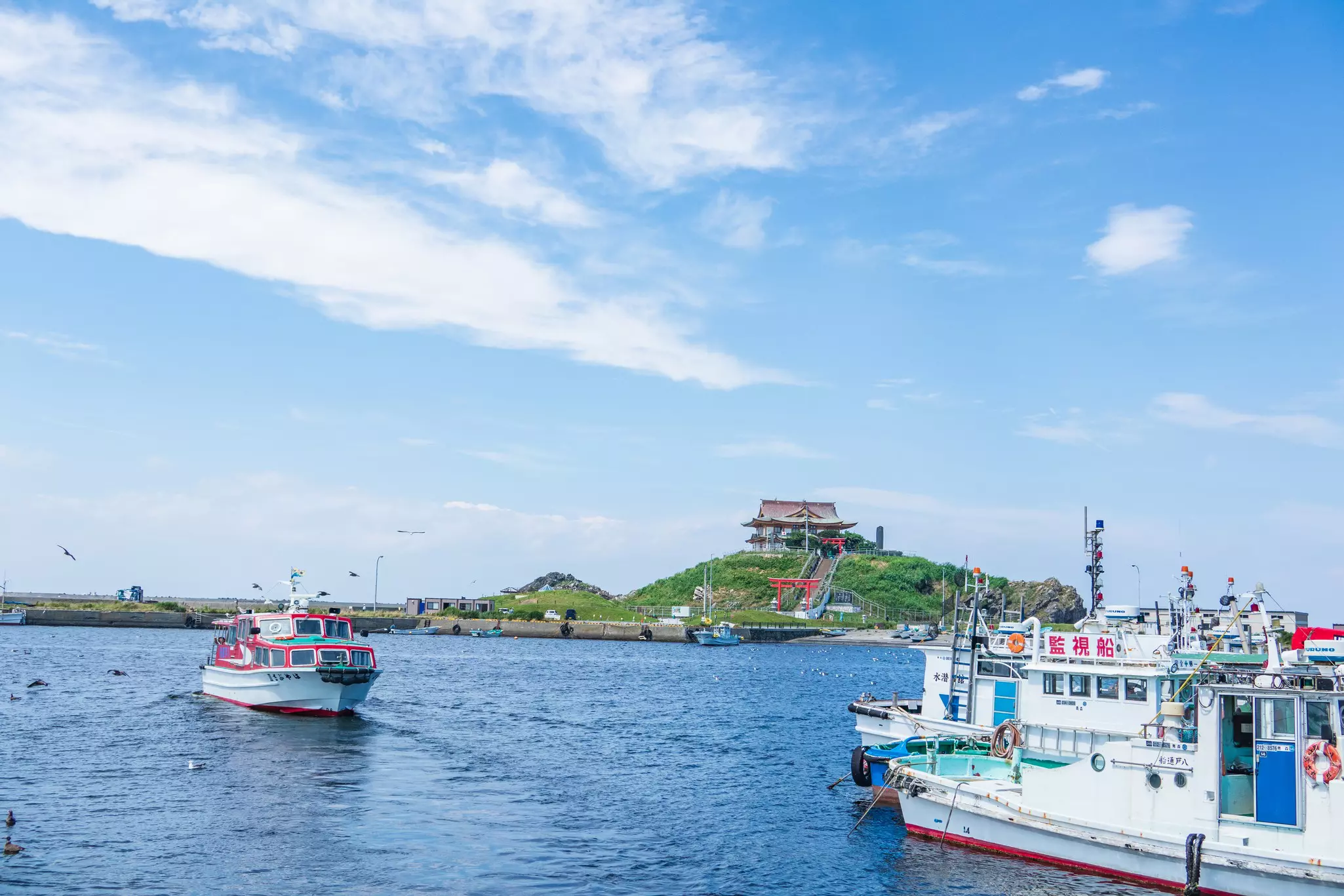 Two small boats in a harbor backed by an island topped with a shrine.