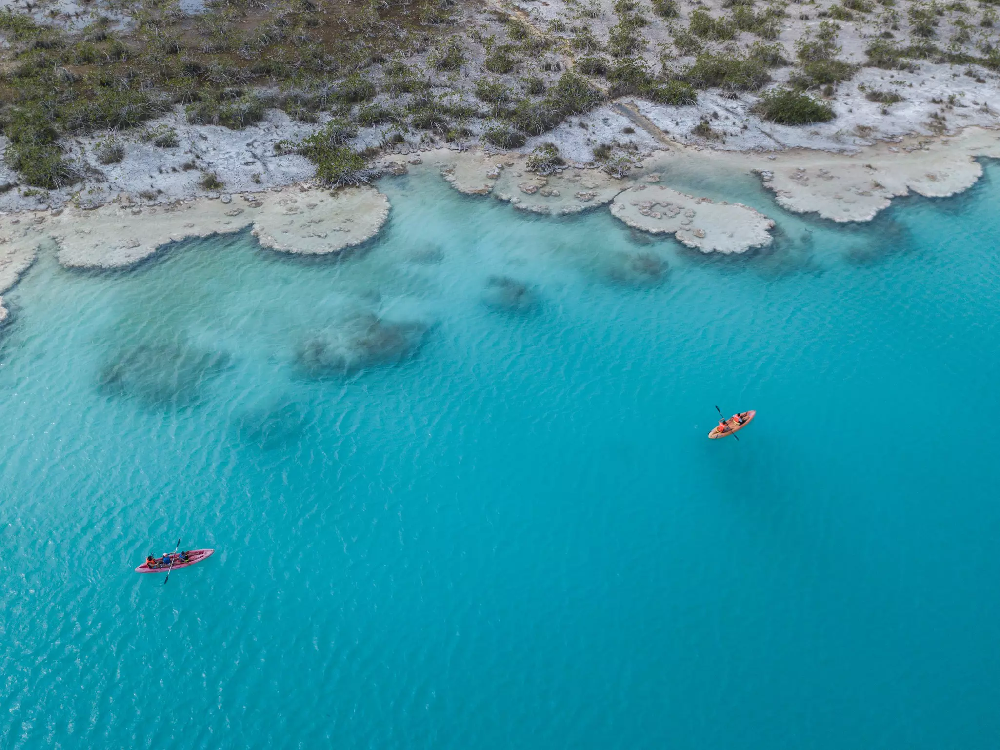 An aerial view of two people kayaking on an azure lagoon.