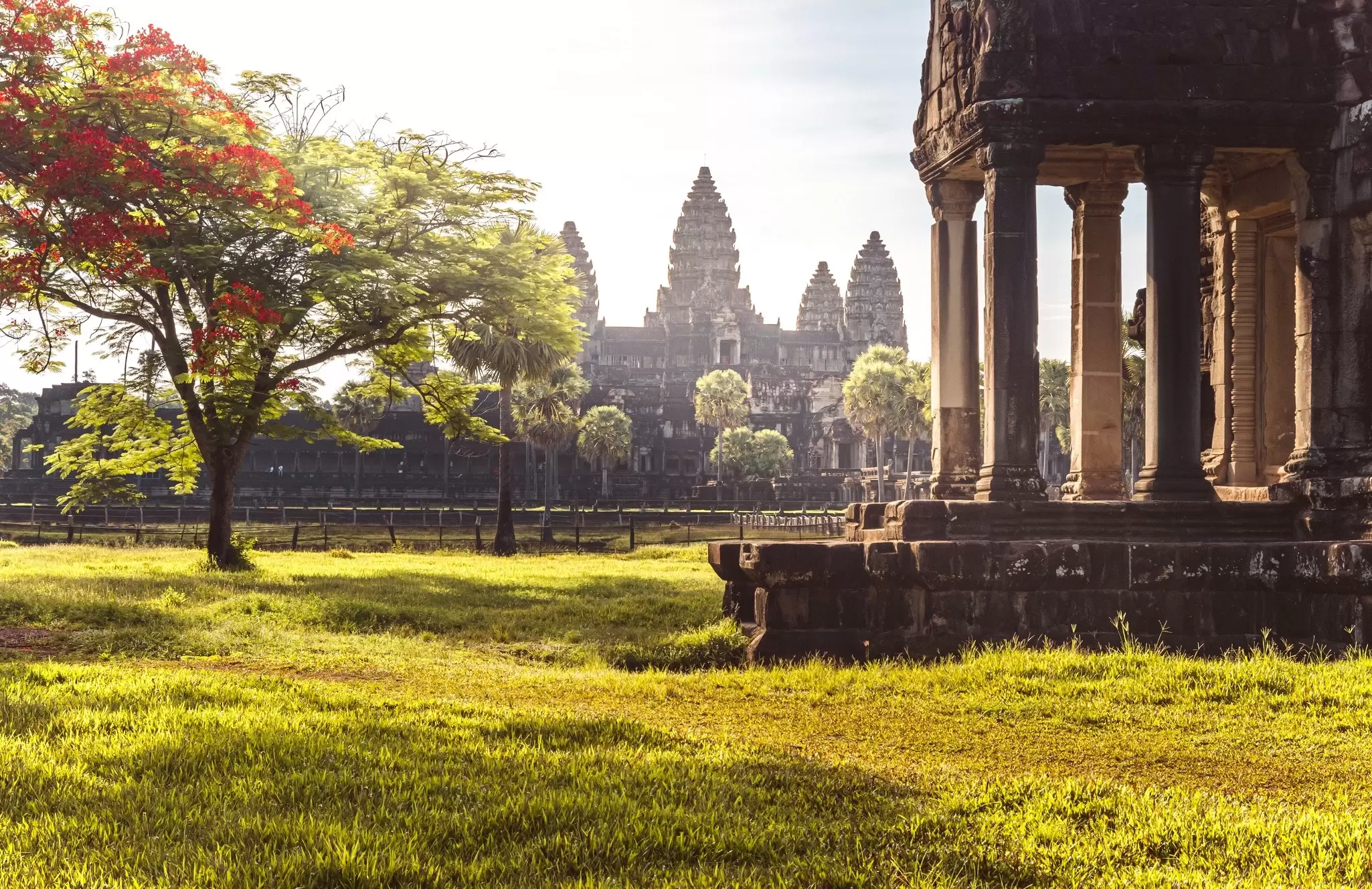 A temple with multiple towers in the background after sunrise; a columned temple is in the foreground.