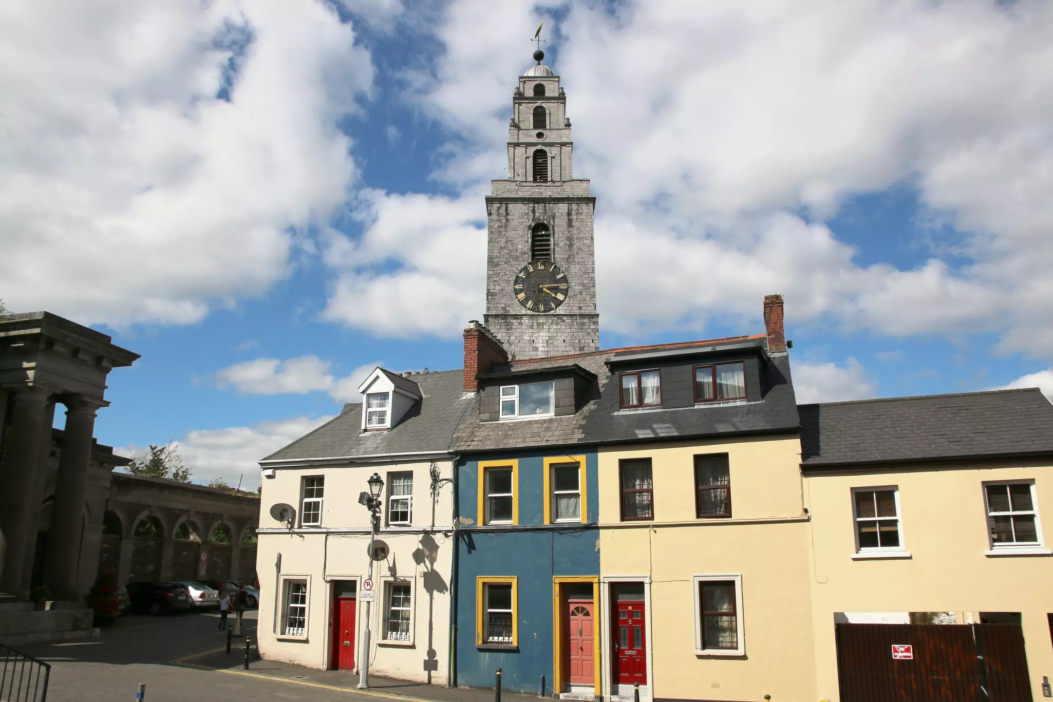 A gray clock tower rises over a stretch of row houses in Cork city, Ireland.