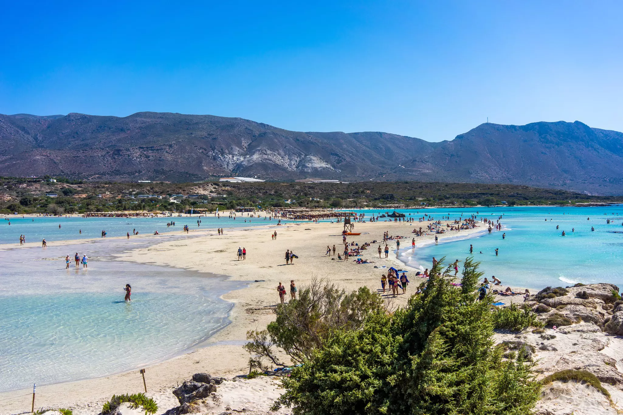 People swim and sunbathe on a beach where a sandbank separates the sea into two
