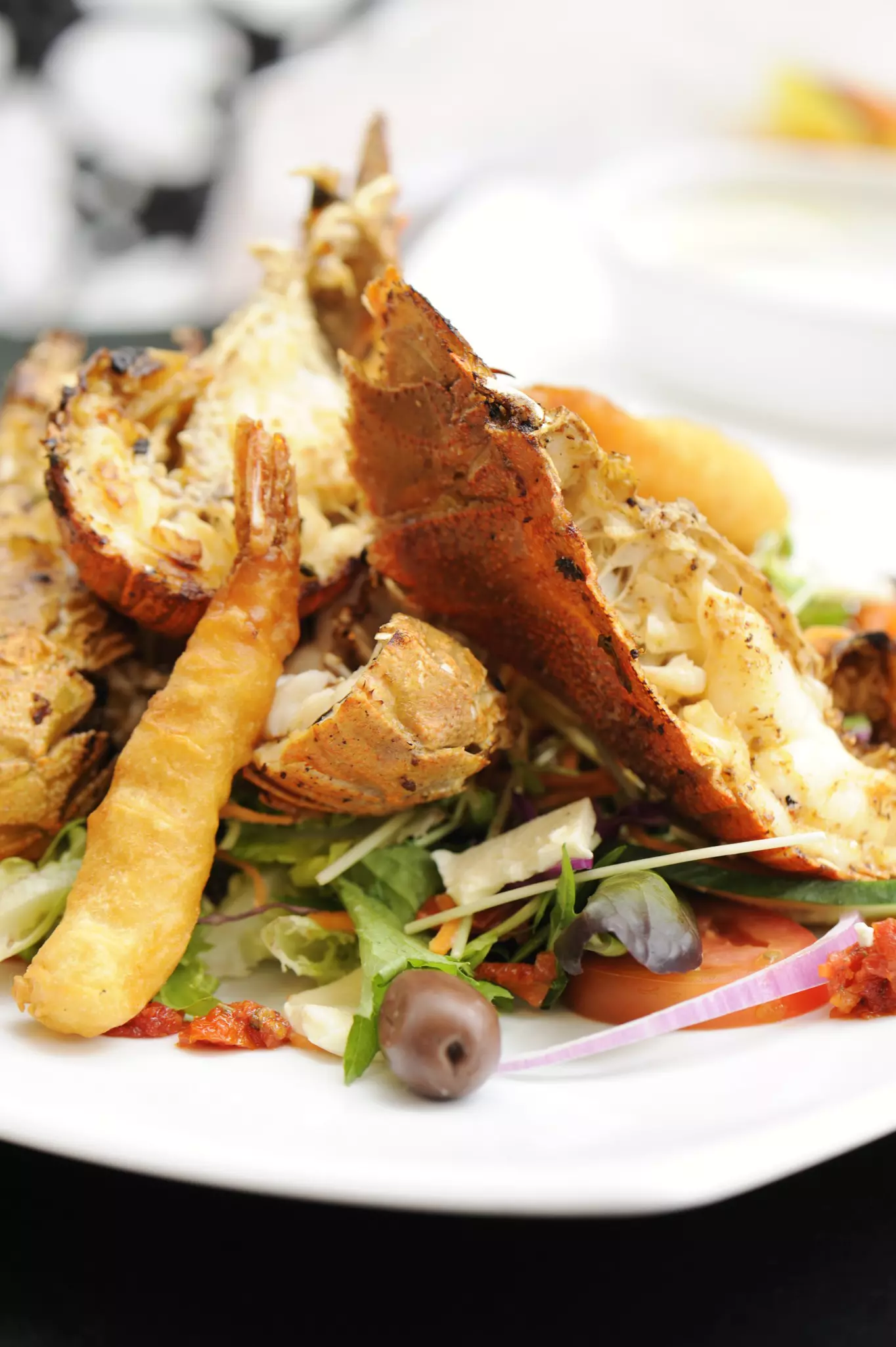 A dish with large crustaceans, similar to lobster, and prawns on top of a salad.