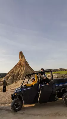 People ride in an open jeep past rock formations.