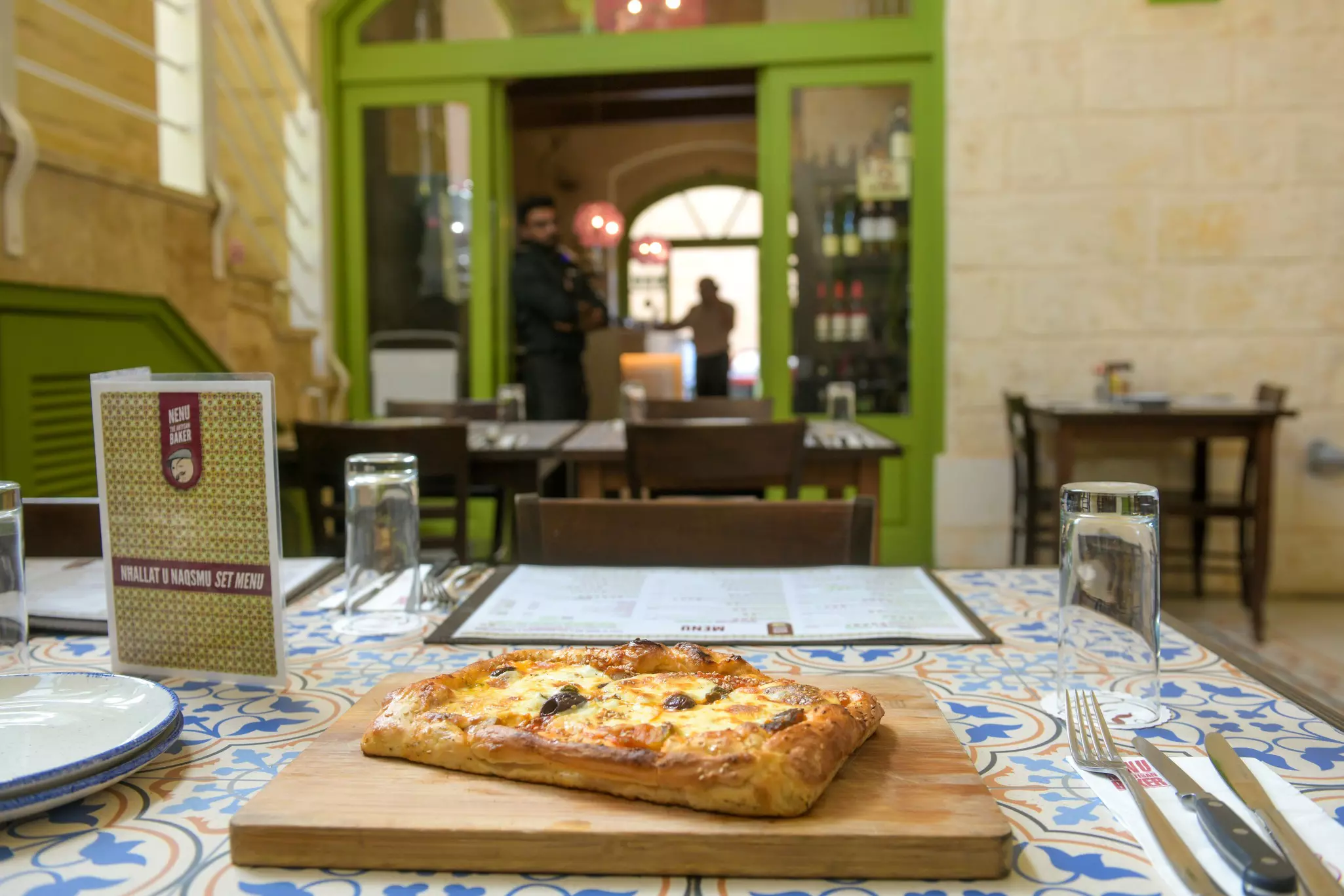 A pizza-like bread dish with melted cheese set on a wooden board on a table in a restaurant.