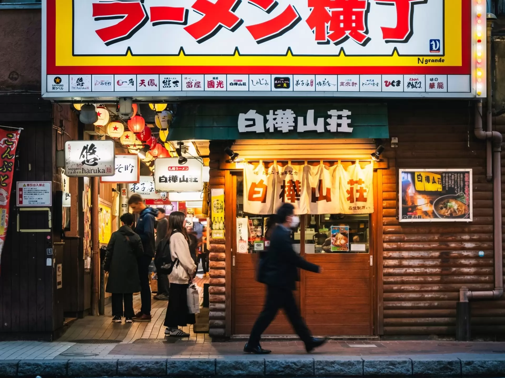 A man walks past a crowded alley lined with small shops selling noodles; Ganso Ramen Yokocho in Sapporo, Japan