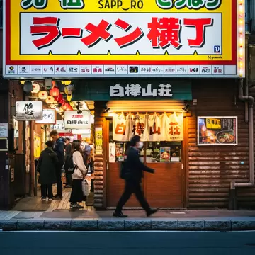 A man walks past a crowded alley lined with small shops selling noodles; Ganso Ramen Yokocho in Sapporo, Japan