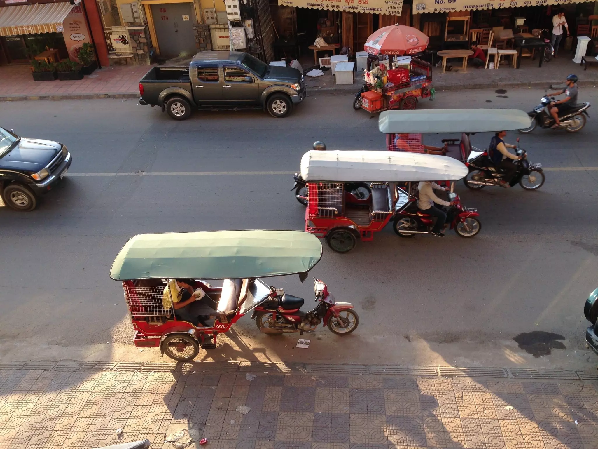 An overhead view of three red tuk-tuks on a city street in Cambodia in the evening.