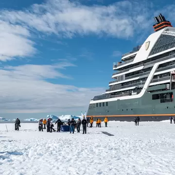 A large cruise ship docked next to an ice shelf with a large group of people standing on it