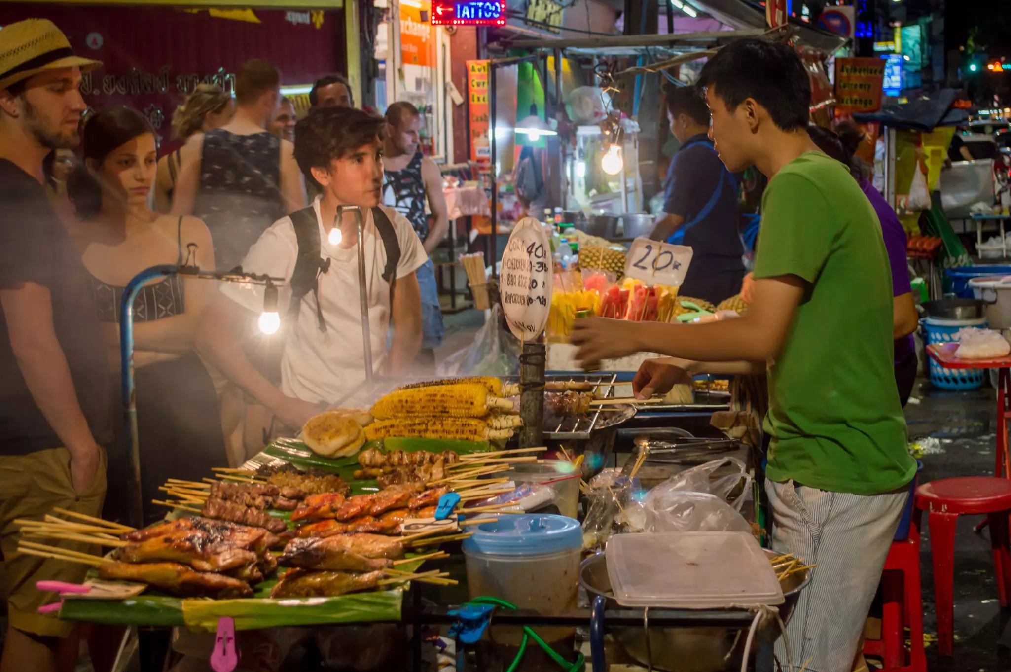 A vendor selling food on skewers to patrons at night in Bangkok.