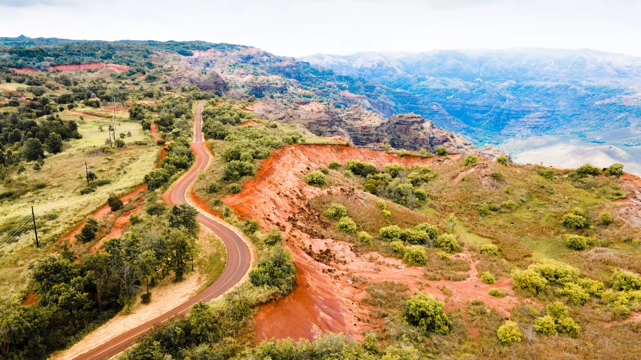 A road winds along the ridge of a hill by rocky outcrops and a valley.