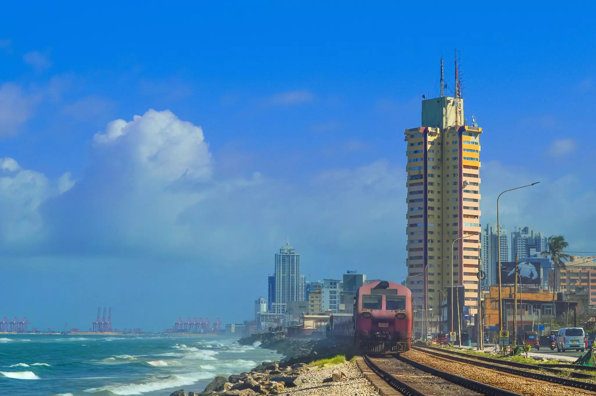 Coastal rail tracks with a train heading away from a city with high-rise buildings.