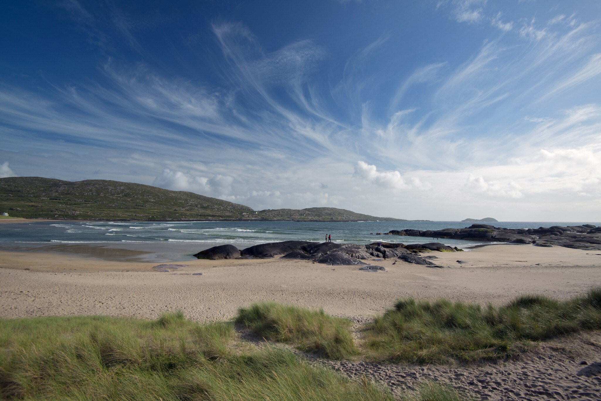 Derrynane Beach on southwest corner of the Ring of Kerry. County Kerry, Ireland. Sweeping blue sky with two figures standing on a rock.