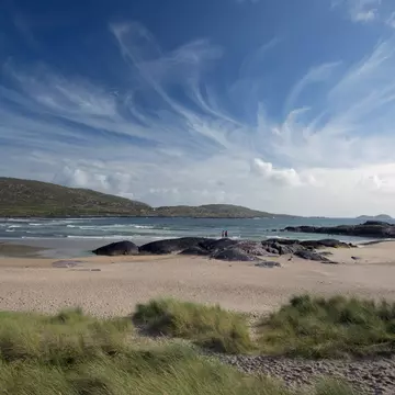 Derrynane Beach on southwest corner of the Ring of Kerry. County Kerry, Ireland. Sweeping blue sky with two figures standing on a rock.